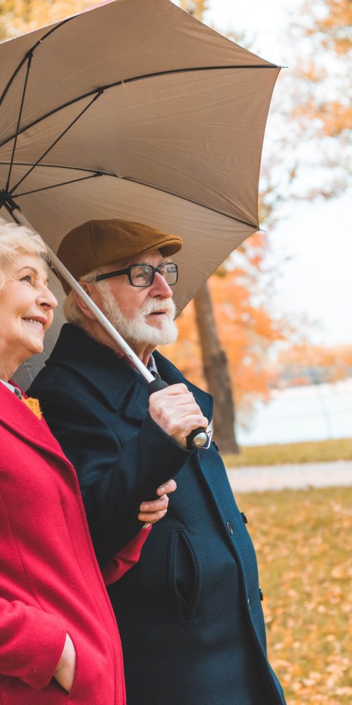 senior couple with umbrella walking in autumn park 2021 08 29 17 02 02 utc min
